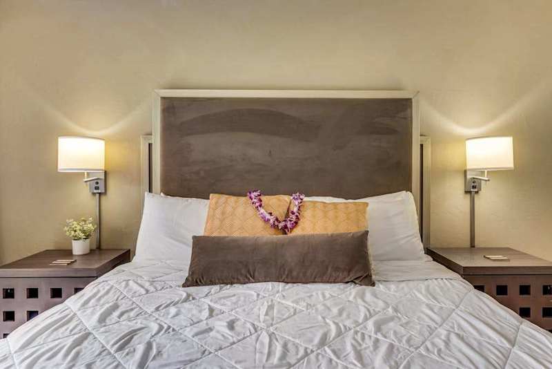 Close-Up View of King Bed with Tufted Headboard, Flower Lei, and Sconce Lighting