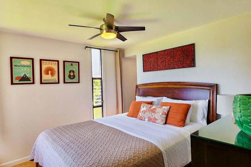 Bedroom features comfortable bed colorful artwork and ceiling fan