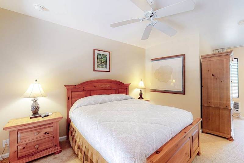 First bedroom features queen bed ceiling fan dresser and lighting
