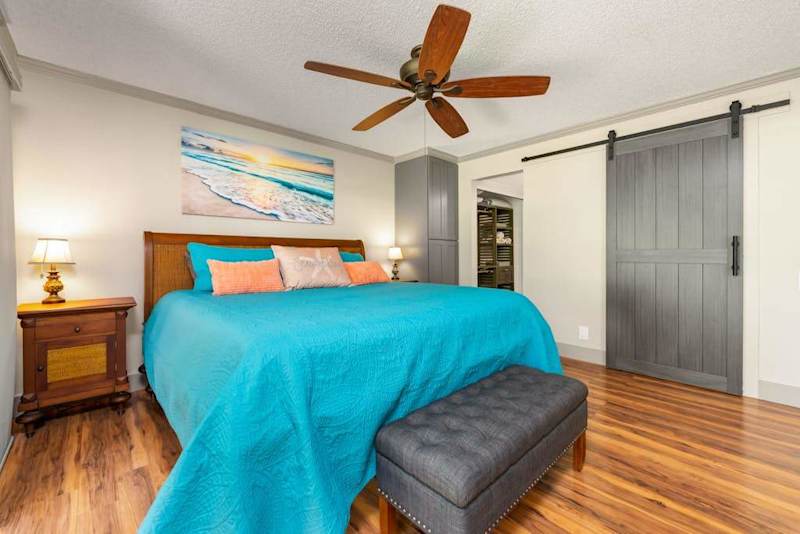 First bedroom showcases colorful bedding warm floors and ceiling fan