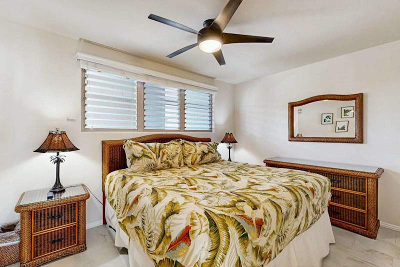 First bedroom features king bed botanical quilt nightstands and fan
