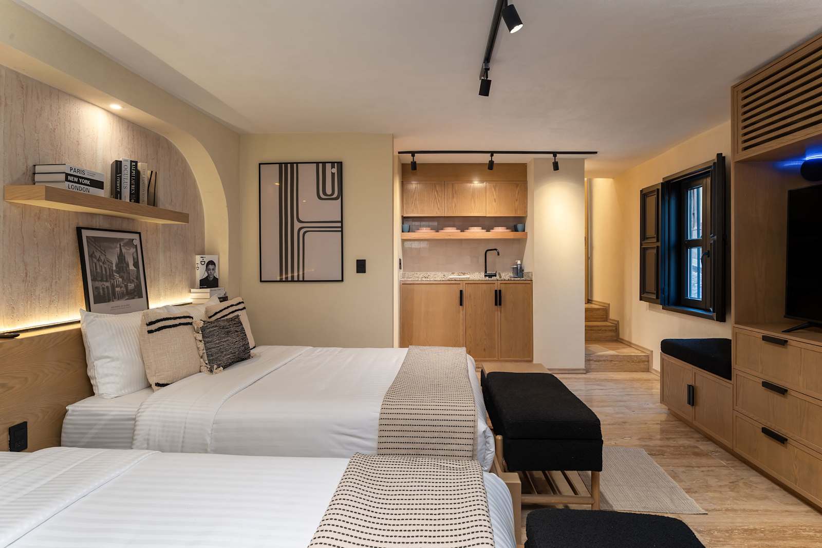Bedroom overview with both queen beds, large windows, wall shelf with framed photos, and a TV with wood built-in dresser and storage.