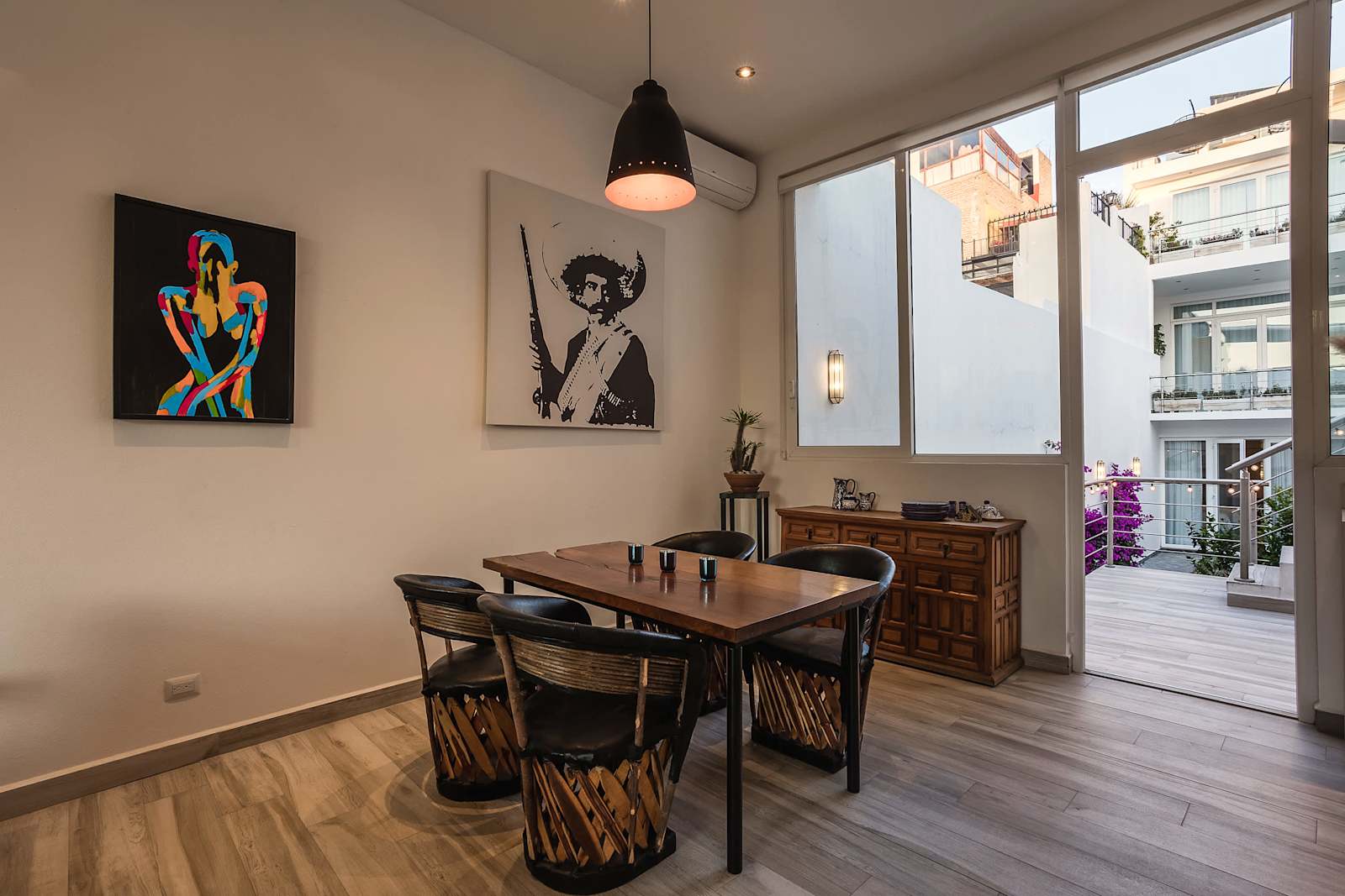 Comedor con mesa de madera, sillas equipales tejidas y acceso a terraza con vista a la ciudad