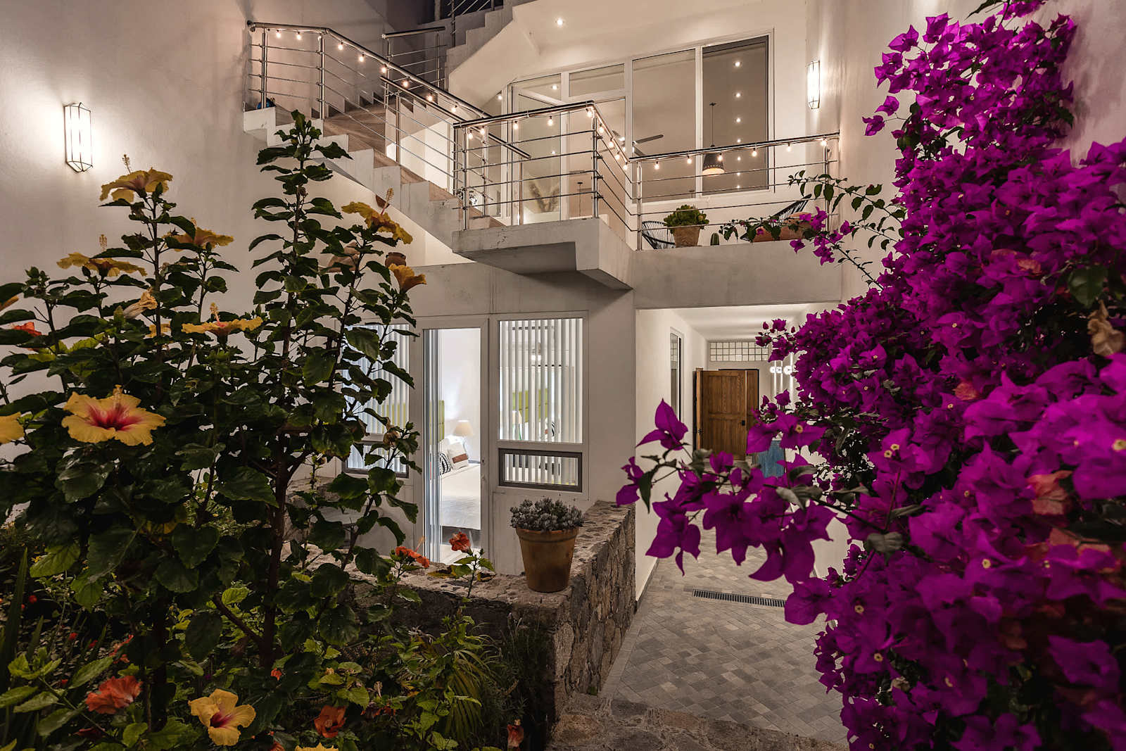 Patio con bugambilia magenta vibrante, flores amarillas y escalera de metal hacia nivel superior