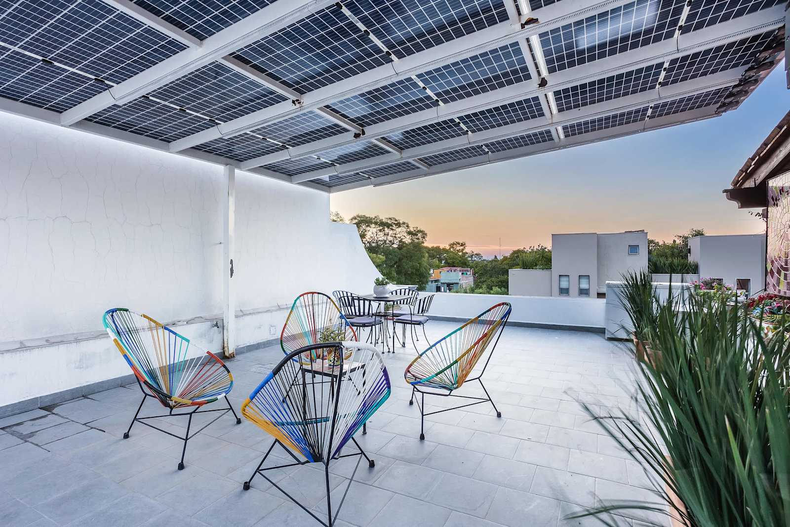 Terraza en la azotea con sillas de colores tejidas, paneles solares y vistas al atardecer sobre las colinas
