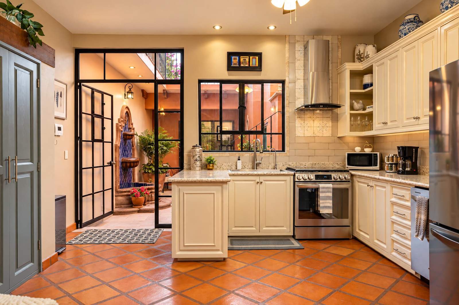 Kitchen with cream cabinetry, terracotta tile floor, and black-framed door to courtyard