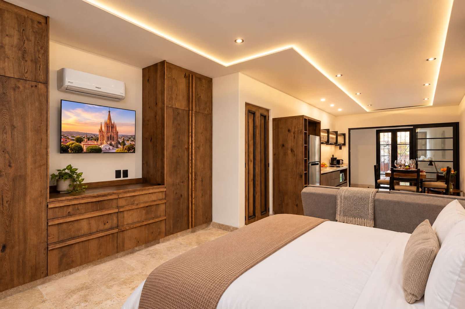 Recámara con cama queen, televisor montado en pared, gabinetes de madera y iluminación LED en el techo
