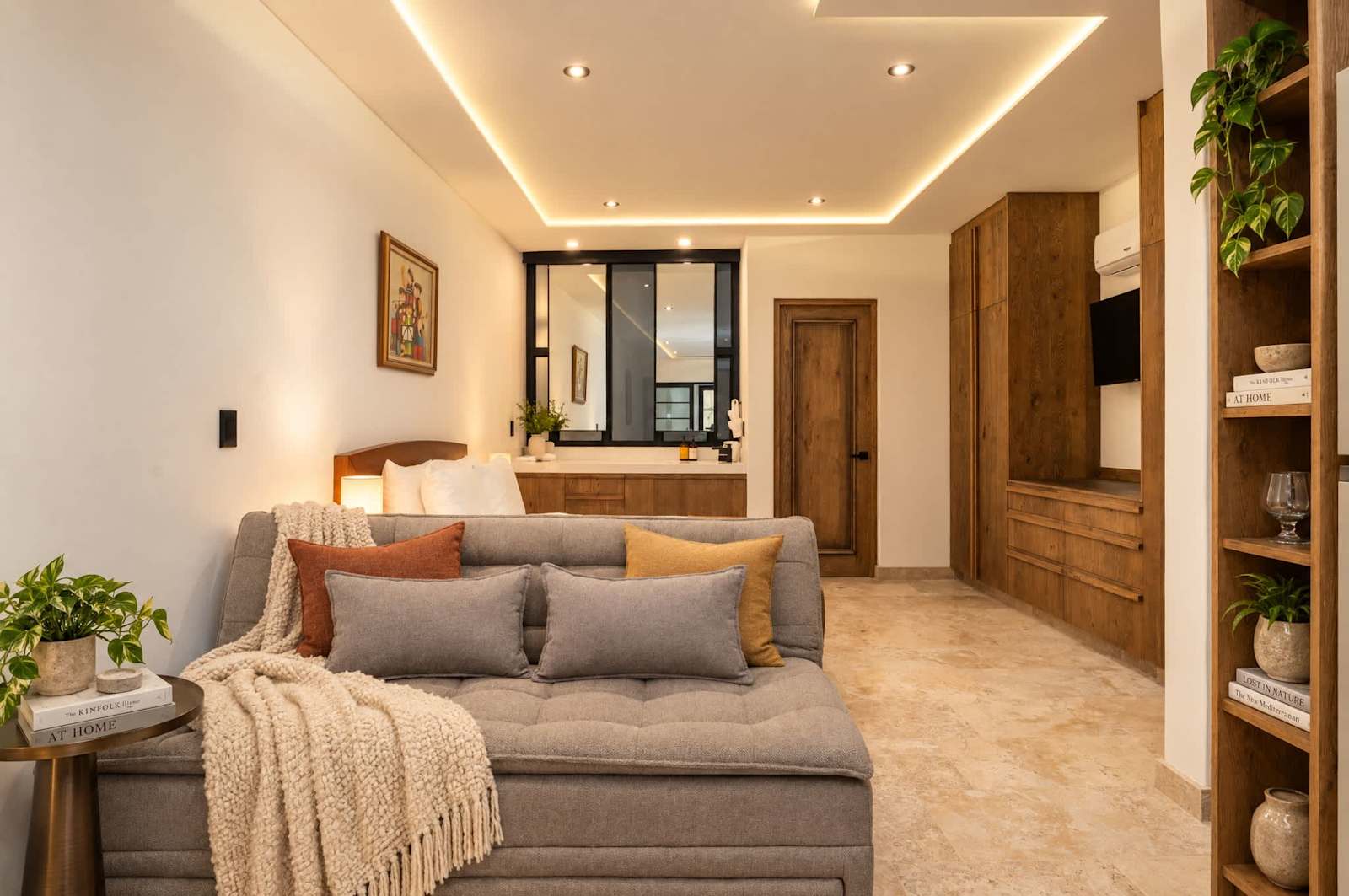 Sala con sofá cama gris, iluminación cálida en el techo y estantes de madera
