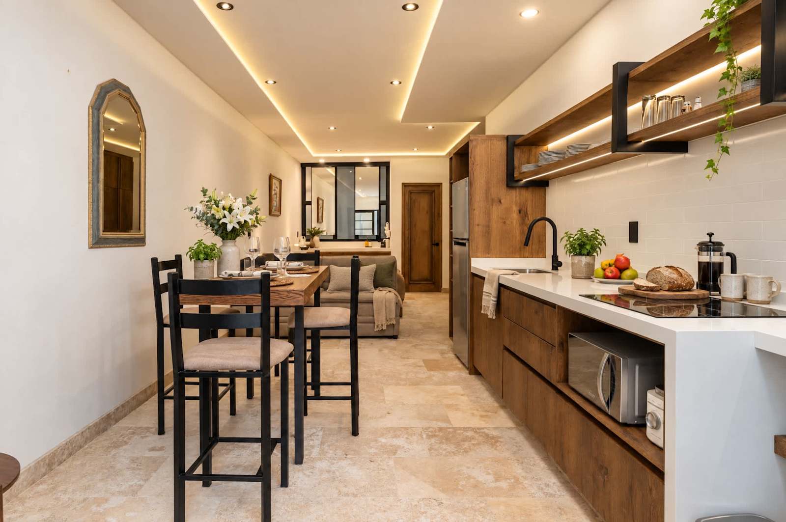 Cocina y comedor de planta abierta con barra, gabinetes de madera y pisos de travertino