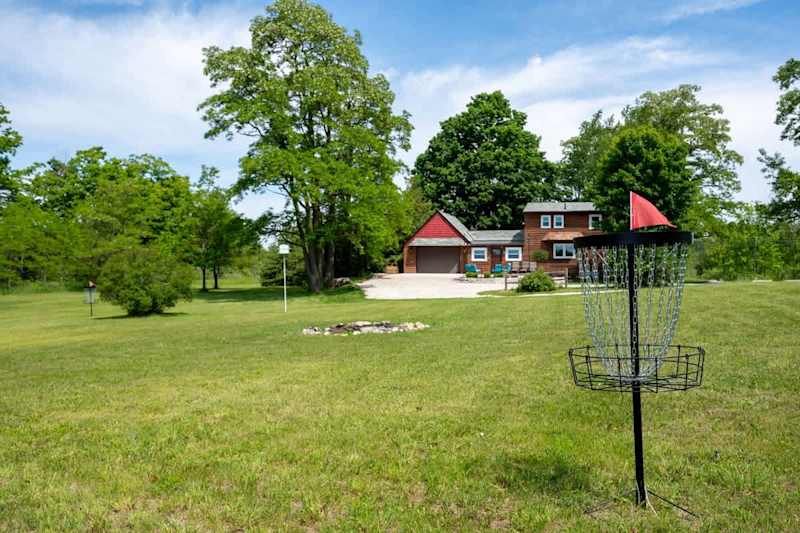 Enjoy the expansive outdoor space at Serenity Acres, complete with a fun disc golf setup and lush greenery. The charming house and well-maintained grounds provide the perfect backdrop for relaxation and outdoor activities.