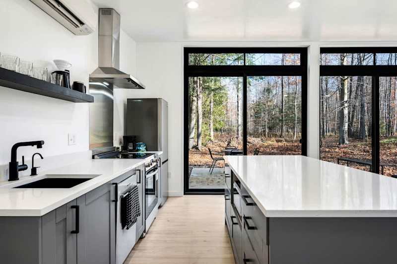 The open-concept living area boasts large floor-to-ceiling windows, flooding the space with natural light and offering picturesque views of the wooded property.