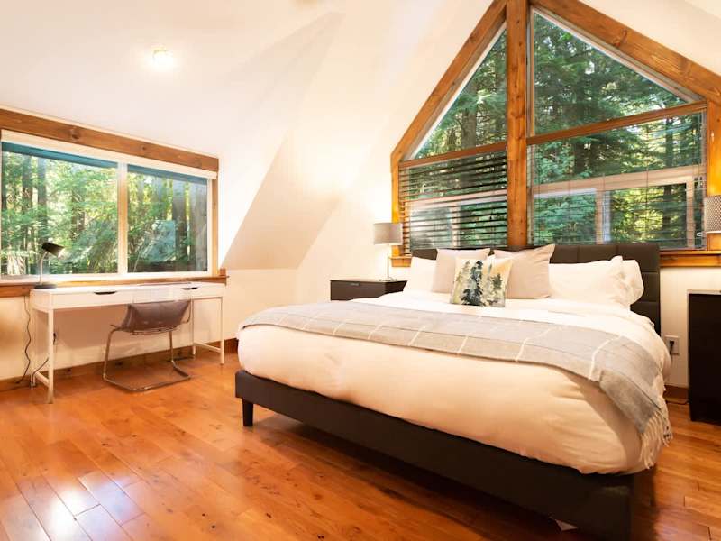 Master bedroom with a comfortable king bed, surrounded by forest drenched windows and a work desk perfect for check ins. 