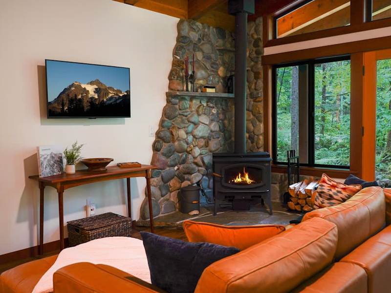 Cozy living room with leather couch, wood burning fireplace with complimentary wood and flat screen TV. 