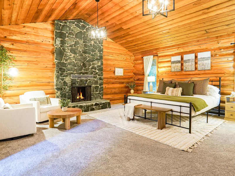 Primary bedroom featuring a Helix king sized bed, cozy seating area, wood burning fireplace, and makeup vanity with mirror. 