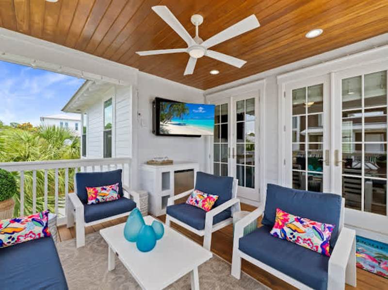 Covered balcony off second floor living area includes ample seating and a smart tv.